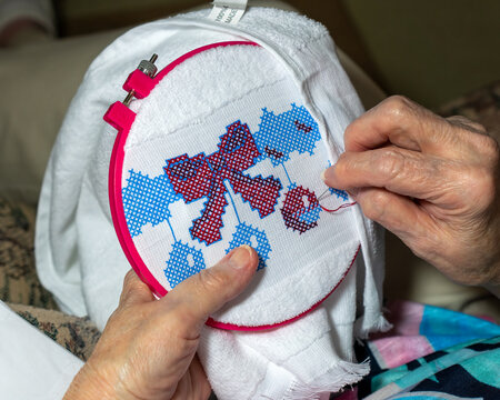 Elderly Woman Sewing A Cross Stitch On A Hand Towel