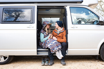 man and woman sat in a campervan enjoying coffee chatting and laughing