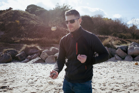 man happily juggling stones on the beach in summer
