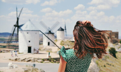 Rear view of a young woman posing against famous old windmills in Consuegra town, Spain - obrazy, fototapety, plakaty