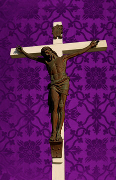 Sun shining on white wood cross with Jesus on Purple silk church parament