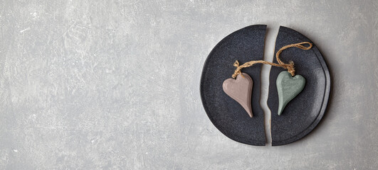 Broken plate and two decorative wooden hearts on a light concrete table