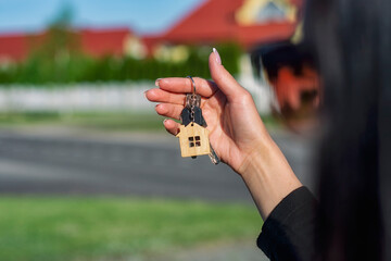 A woman holds in her hands the keys to the house against the background of residential buildings. Concept for buying and renting apartments.