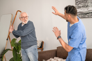 Aggressive pensioner brandishing the walking stick at his caretaker - obrazy, fototapety, plakaty