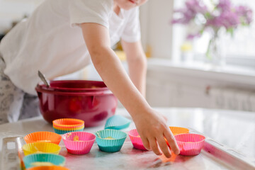 Little kid 5 years old cooks cupcakes in light kitchen at home. Little boy uses silicone baking...