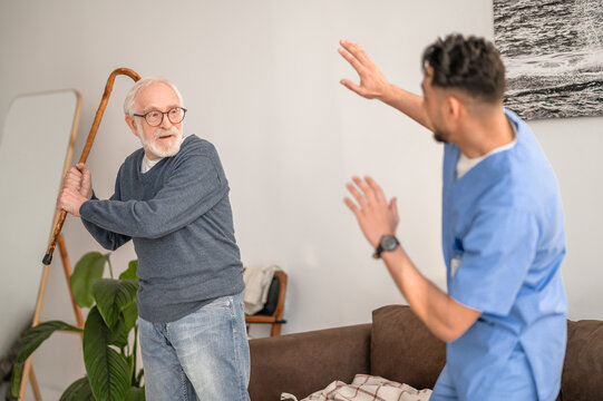 Aggressive pensioner brandishing the walking stick at his caretaker