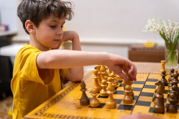 Brunette boy playing a game of chess on large chess board at home.