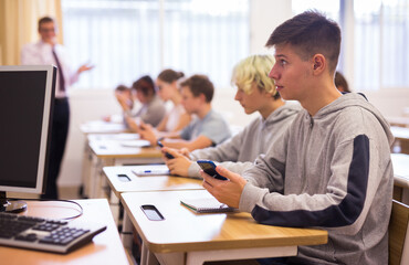 Fototapeta premium Confident teen students using social media on phones while studying in high school