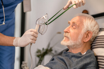 Medical worker preparing a bedridden aged man for oxygenation