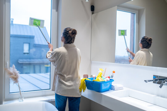 Young woman cleaning the window in the bathroom