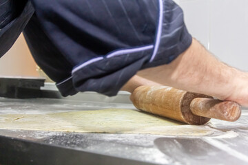 Hands work with the dough to make fresh Italian pasta. Women's hands make dough for homemade pizza on a wooden table strewn with flour .