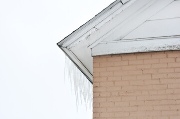 Icicles on wooden roof edge of brick building against overcast snowy sky