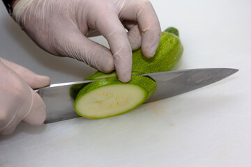 A portrait of a person cutting a courgette with a sharpp knife in a kitching while cooking a nice...