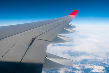 Fototapeta premium View from passenger cabin window on wing of flying plane against background of blue sky and white clouds