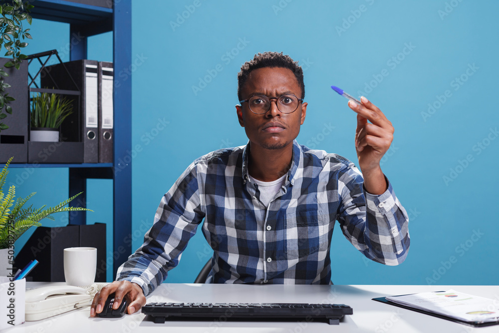 Poster pov of unsure suspicious office administrator having pen in hand looking mistrustful at computer mon