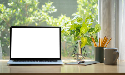 Computer laptop with empty display, coffee cup, pencil holder and houseplant on wooden table.