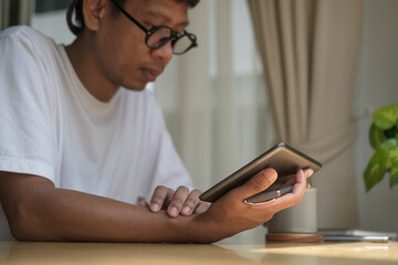 Young Asian man sitting on comfortable and using digital tablet.