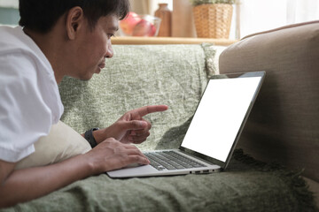 Asian man lying on couch and using laptop computer, surfing internet, working online.