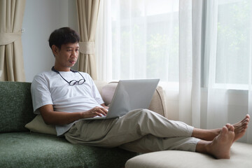 Happy young man sitting on couch in living room and using laptop computer.