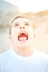 portrait of a preteen boy with his mouth wide open showing his tongue and teeth in a craziness...