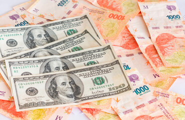 Fototapeta na wymiar Hundred dollar bills over an amount of devalued Argentine pesos.
