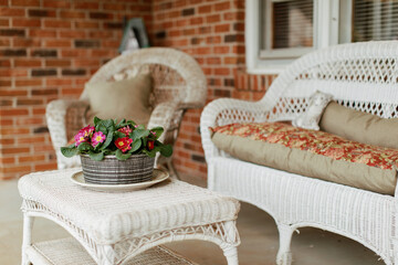 Front porch white whicker furniture and potted flowers on a red brick front porch