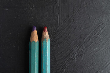 close up de puntas de dos lápices de color rojo carmín y morado desgastadas sobre fondo negro de...
