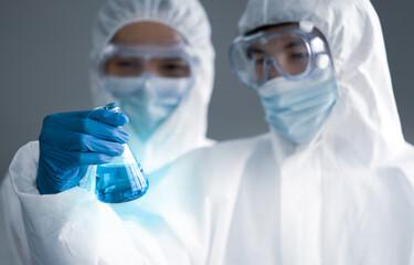 Covid-19 testing in laboratory. Two Scientists discuss about blue liquid chemical in Erlenmeyer...