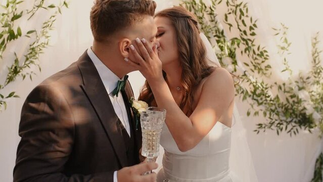 groom and bride in dress kiss hugging each other. Wedding ceremony for newlyweds in Europe in a classic minimalist style in nature against the backdrop of an arch covered with silk fabric fresh plants
