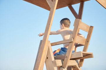 Elementary age skinny boy plays being a simulated life guard during the summer holidays on top of...