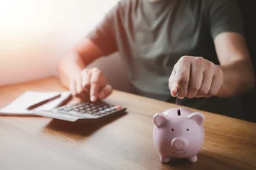 Fotobehang A man hand putting coins in pink piggy bank for account save money. Planning step up, saving money for future plan, retirement fund. Business investment-finance accounting concept. © otello-stpdc