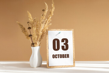 october 3. 3th day of month, calendar date.White vase with dried flowers on desktop in rays of...
