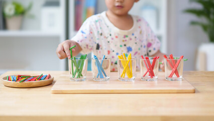 Unidentified hands of little boy learning to sorting the color rod to the glass, concept of homeschool, montessori, freedom, education, activity for child development and sensory activity for kid. - obrazy, fototapety, plakaty