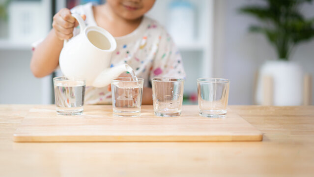 Unidentified hands of little child pouring the water to the cup in montessori class, concept of homeschool, practical life skill, kid learning activity, freedom, education for kid development.
