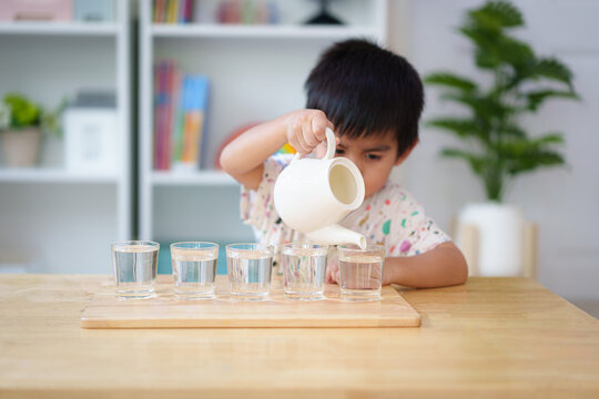 Blurred of 3 years old asian little boy pouring the water to the cup in montessori class, concept of homeschool, practical life skill, kid learning activity, freedom, education for kid development.
