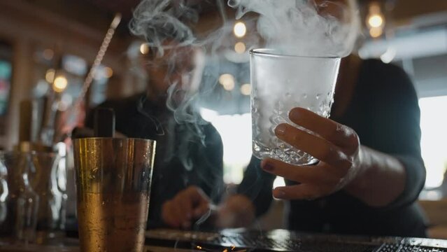 Lifting glass from burning wood chips with smoke escaping for cocktail