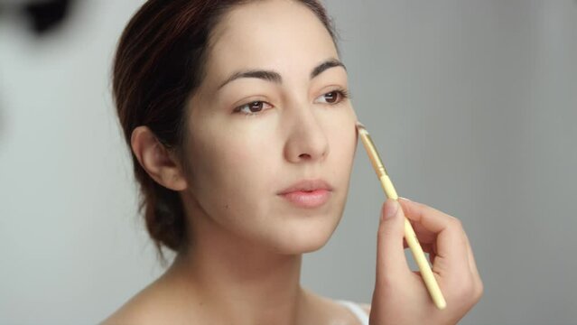 Makeup tutorial: Side view, lovely brunette woman applies foundation with brush