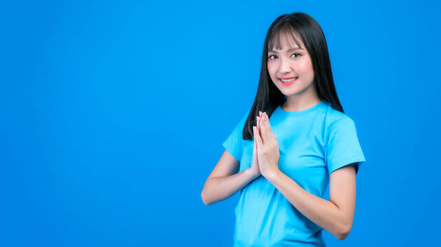 Portrait beautiful Asian young woman bangs hair style pay respect , sawasdee symbol from Thailand greeting culture for hello or goodbye isolated on blue background