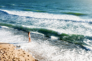 Young woman with beautiful body standing on the beach at sunset and looks into the distance. Summer vacation, sunny concept