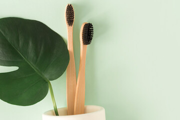 Zero waste concept. Top view natural eco bamboo toothbrush with monstera leaves on green background,  top view. Copy space