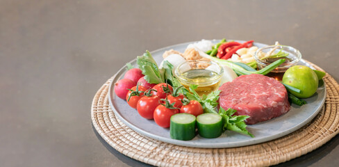 The uncooked ingredients prepared for making yum steak, spicy Thai salad style, are arranged and placed on a local tray set.