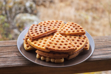 A plate of triangular sweet waffles stands on the wooden railing of the gazebo. Tourist food. Home baking in the country.