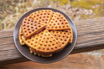 A plate of triangular sweet waffles stands on the wooden railing of the gazebo. Tourist food. Home baking in the country.