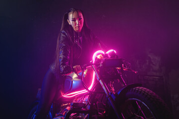 Fototapeta na wymiar Girl a motorbiker near the old motorcycle in the neon lights.