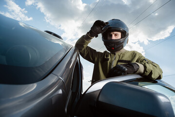 Rally driver concept. Young man i a suit and helmet is standing near the car on a countryside road.