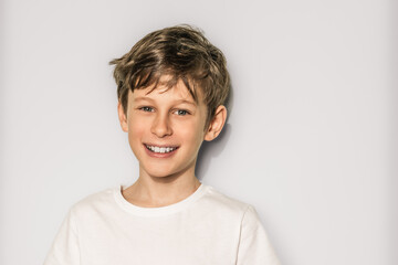 Portrait of a handsome smiling 9 year old white caucasian boy in a white t-shirt on a white background with copy space