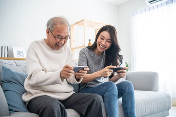 Asian senior father and daughter play game on phone together in house. 