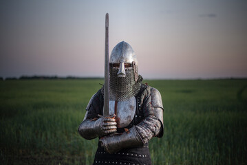 Knight guardian armor with a sword in hands stands in the field on a sunset background. The kingdom...