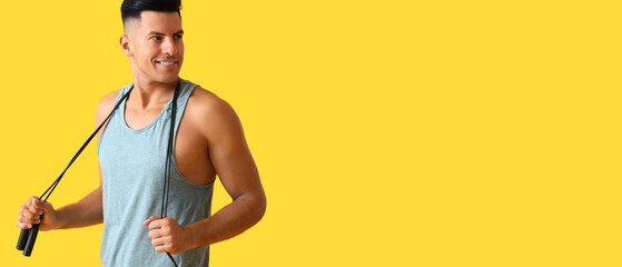 Sporty young man holding skipping rope on yellow background with space for text