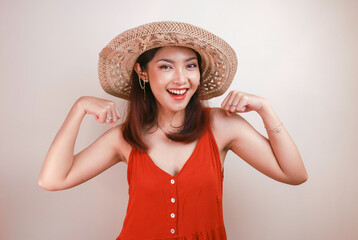 Gorgeous strong young Asian woman with orange dress and straw hat showing biceps and smiling....